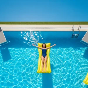 An overhead view of a person peacefully relaxing on a floating water mattress in a swimming pool on a sunny day.